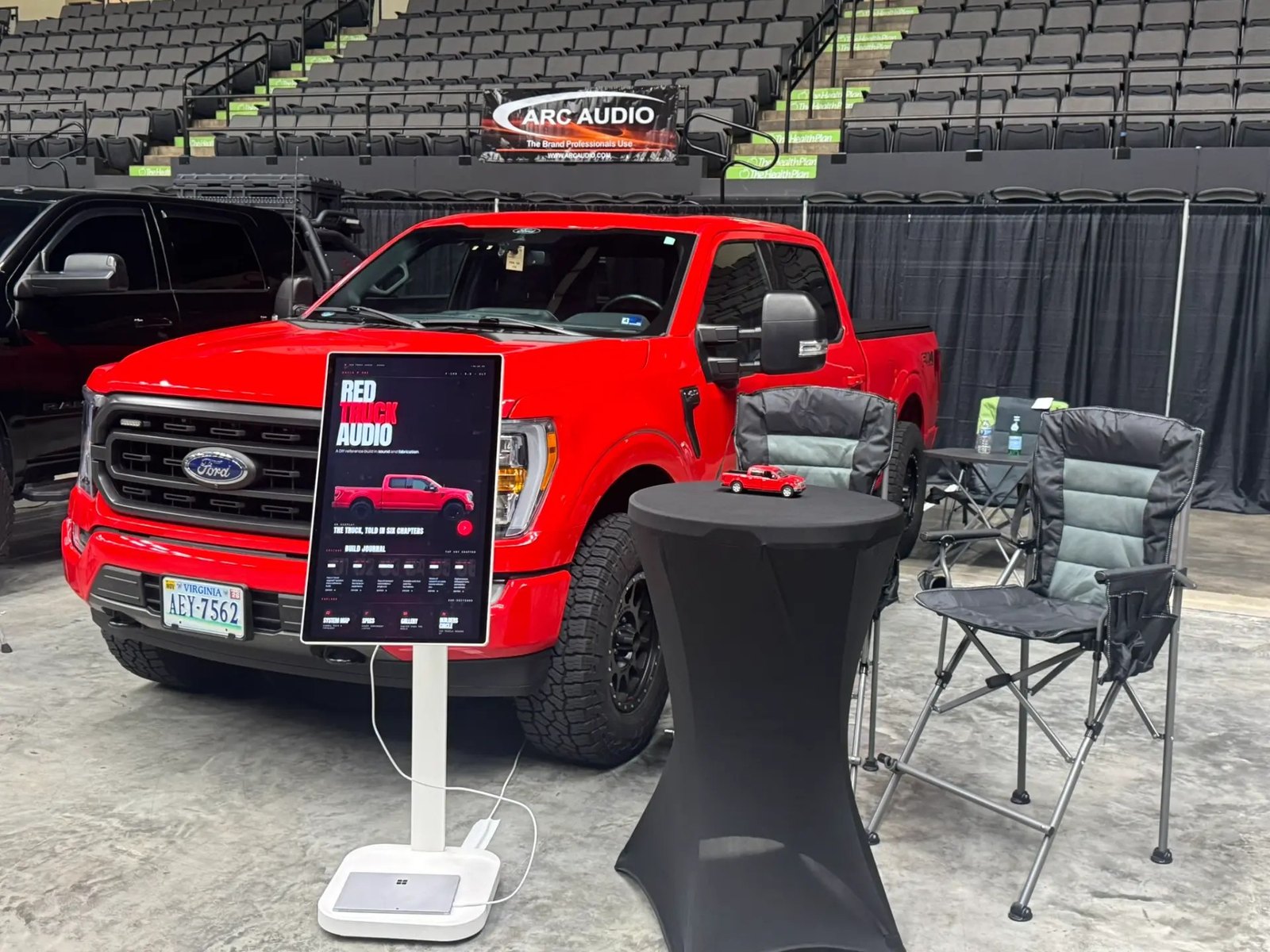 Wide shot of the Red Truck Audio kiosk in the competition hall, with the red F-150 and stadium seating behind it